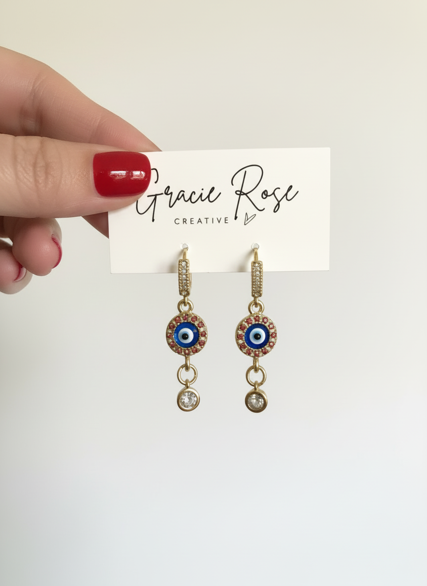 Stylish Evil Eye Luxe Drop Huggie earrings showcasing a radiant gold design with a charming evil eye and shimmering accents.