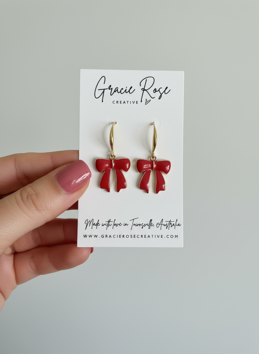 Cherry Bow Dangles earrings by Gracie Rose Creative shown on a business card. Featuring handmade classic red bows with gold hooks, ideal for gifting or personal style.