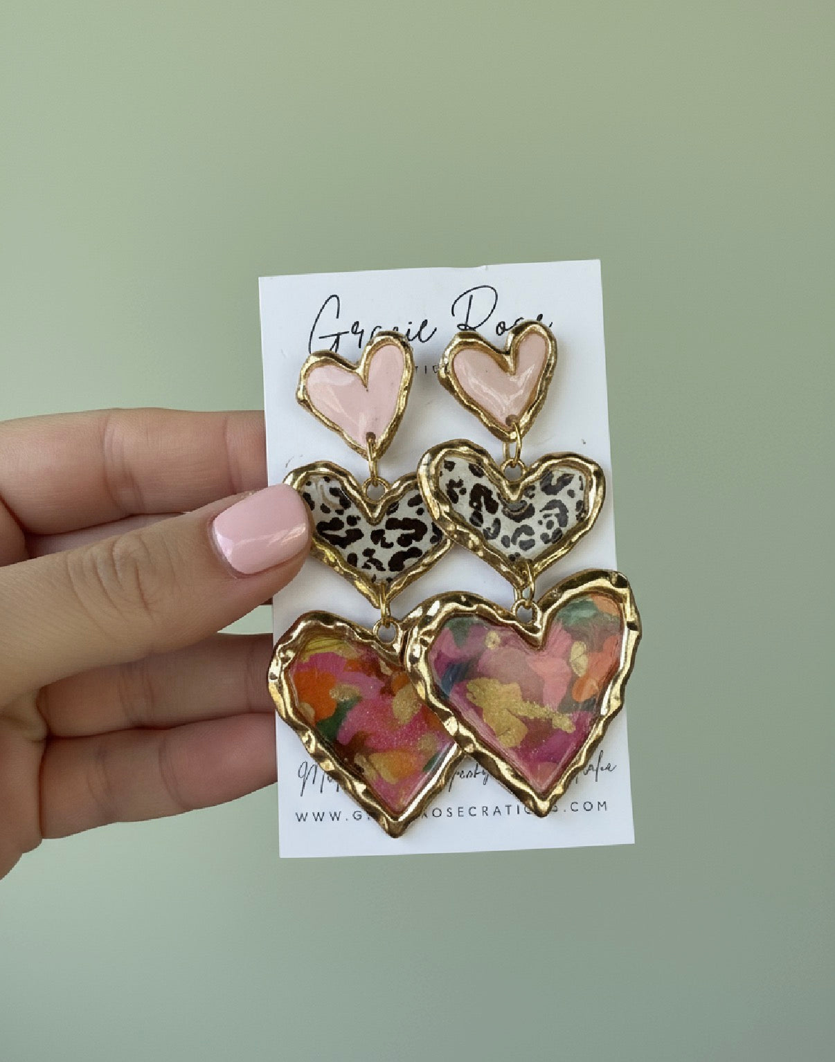 Hand holding Cross Your Heart pink floral earrings by Gracie Rose Creative, displaying the beautiful craftsmanship and colorful heart shapes.