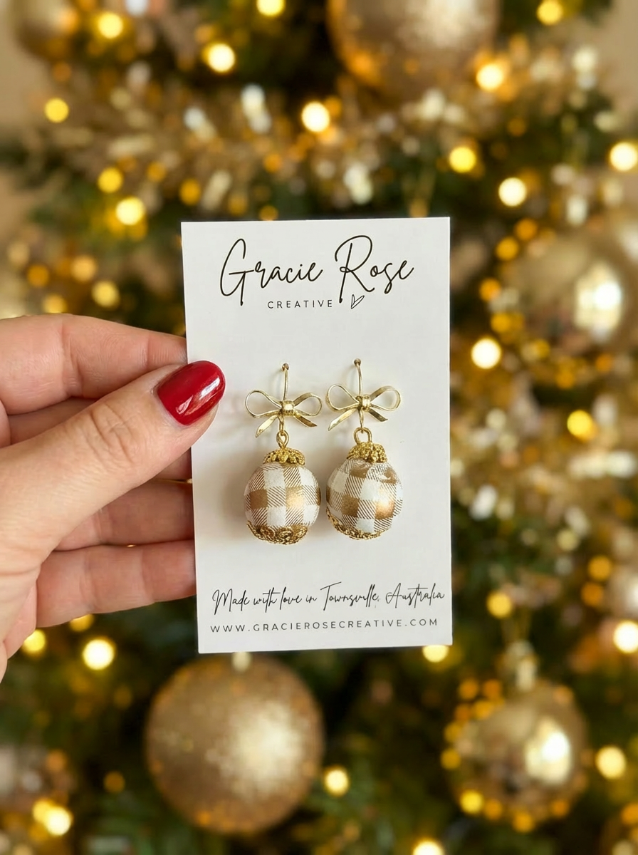 Close-up of Gingham Baubles earrings by Gracie Rose Creative held against a background of sparkling Christmas lights, showcasing their unique gingham print and gold accents.