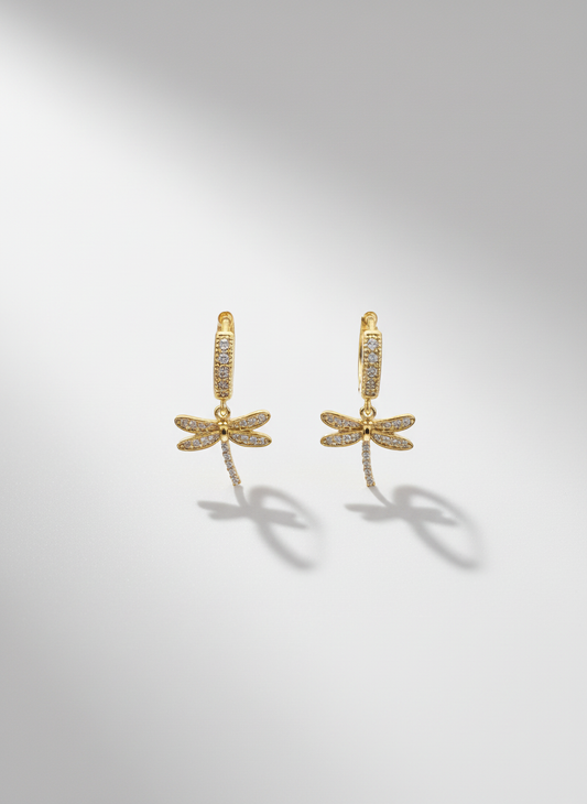 Close-up of Dragonfly Drops by Gracie Rose Creative, showcasing delicate gold huggies with sparkling dragonfly charms against a soft background.