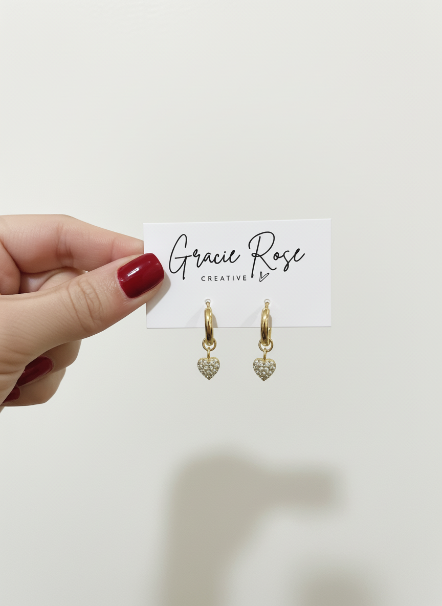 Hand holding Luxe Love Huggies by Gracie Rose Creative, displayed on a branded card, emphasizing the stylish gold earrings.