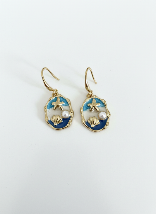 Handmade gold-toned earrings from Gracie Rose Creative called The Blue Horizon, featuring ocean-blue enamel, a pearl, starfish, and shell details.