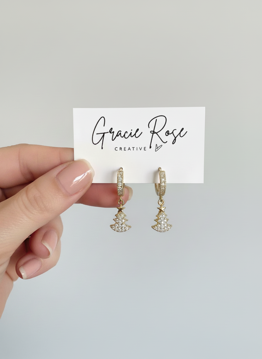 Twinkle Tree Huggies by Gracie Rose Creative displayed elegantly in a hand, highlighting the glittering Christmas tree charms and gold-plated design.