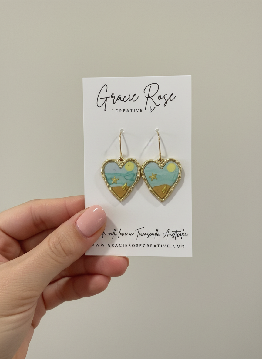 Display of 'Seaside Sweetheart' earrings by Gracie Rose Creative held up, highlighting their unique design with ocean blue and sandy hues.