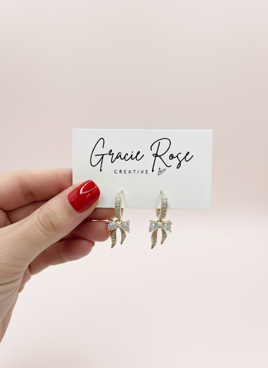 Hand holding The Crystal Bows earrings by Gracie Rose Creative with a stylish brand card, highlighting their luxurious design.