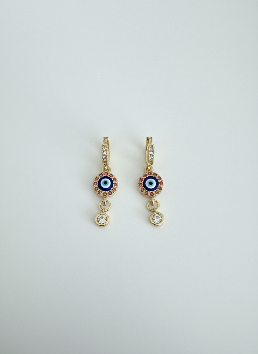 Evil Eye Luxe Drop Huggie Earrings featuring gold-tone huggie hoops, sparkling evil eye charm detail, and crystal drop accent, perfect for stylish and protective everyday wear.