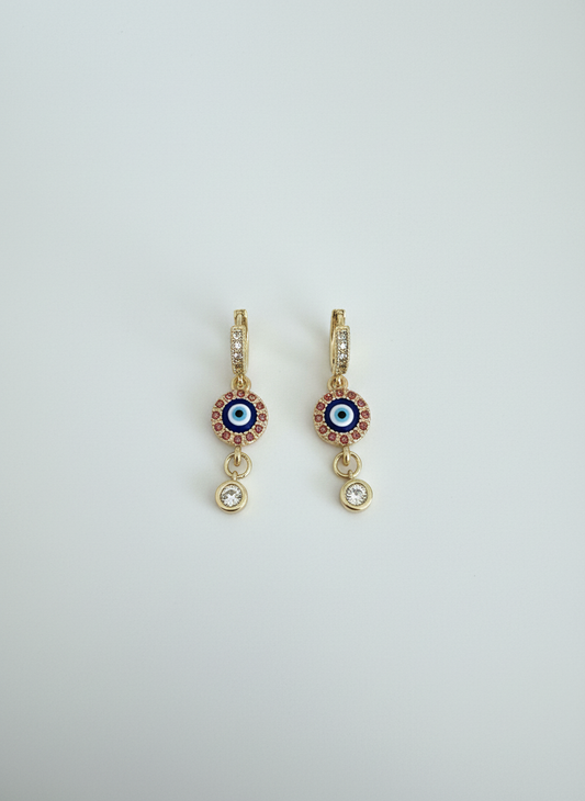 Evil Eye Luxe Drop Huggie Earrings featuring gold-tone huggie hoops, sparkling evil eye charm detail, and crystal drop accent, perfect for stylish and protective everyday wear.