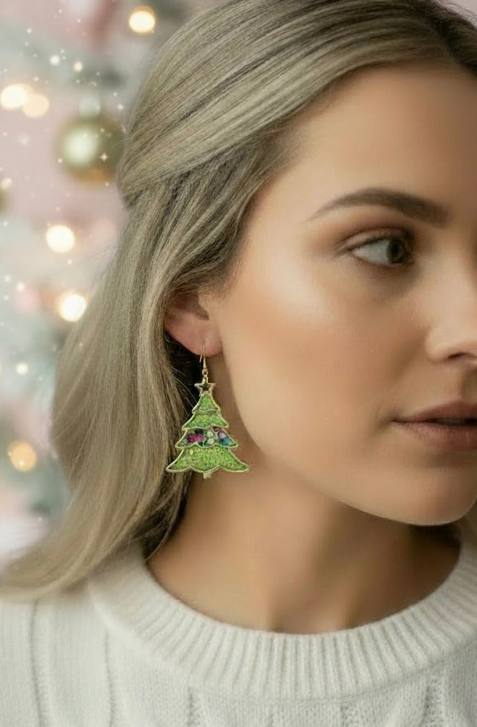 Model wearing Oh Christmas Tree… green earrings by Gracie Rose Creative, showcasing a festive tree design against a blurred holiday background.