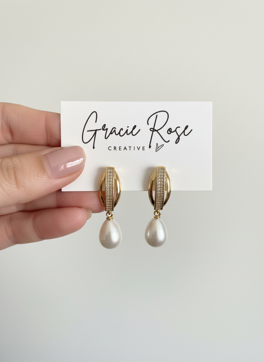 Handholding Timeless Pearl Huggies by Gracie Rose Creative, highlighting the beautiful craftsmanship and design of the pearl drop earrings.