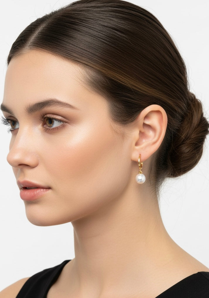 A model wearing the Classic Pearl Huggies by Gracie Rose Creative, elegantly displays these pearl and gold earrings. Their delicate dangle design makes them perfect for chic gold jewelry, bridal accessories, or summer jewelry, combining sophisticated style with minimalist elegance for a refined look.
