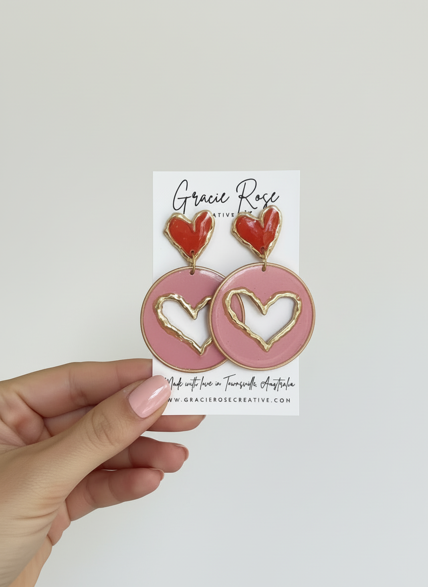 Pink circle earrings with gold heart cut-outs and red heart stud presented by hand, made by Gracie Rose Creative - Candy Hearts 2.0.