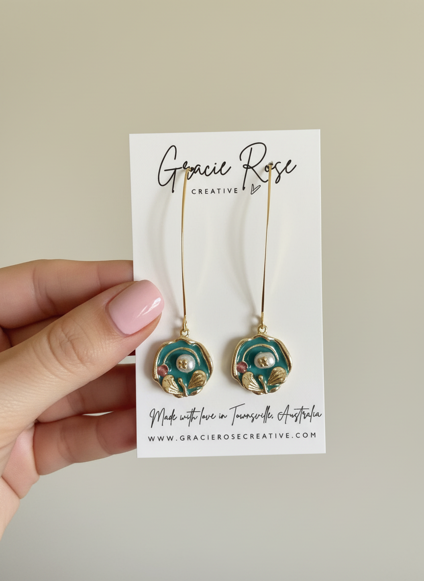 Heirloom Bloom earrings by Gracie Rose Creative showcased on a display card, featuring teal tones and gold detailing with a pearl center.