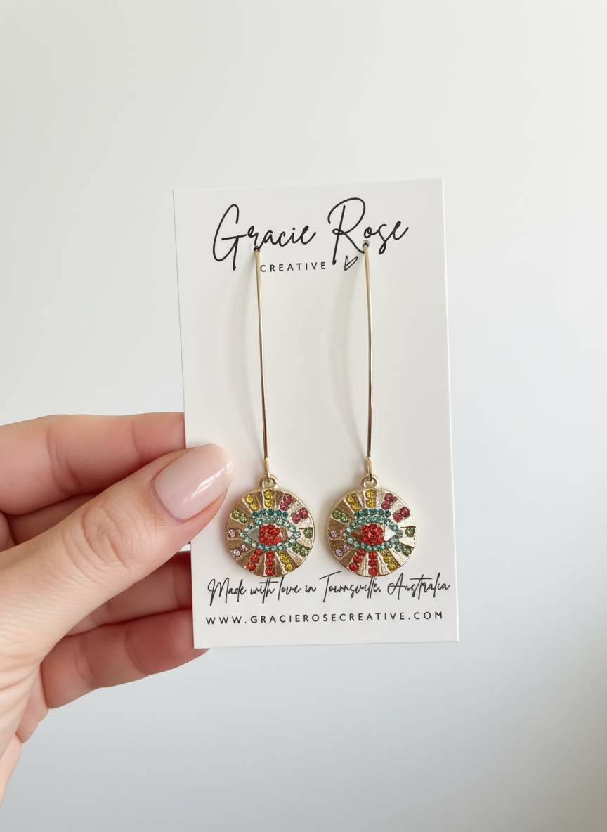 Hand holding Prism Protector Earrings by Gracie Rose Creative, displaying the colorful crystal details and branding card.