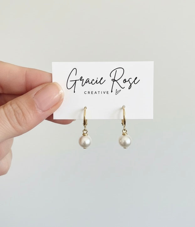 A hand holding the Classic Pearl Huggies by Gracie Rose Creative emphasizes their unique handmade jewelry appeal. These luxurious gold dangle earrings with pearls are the perfect gift for her, symbolizing summertime elegance or romantic jewelry ideal for date night.