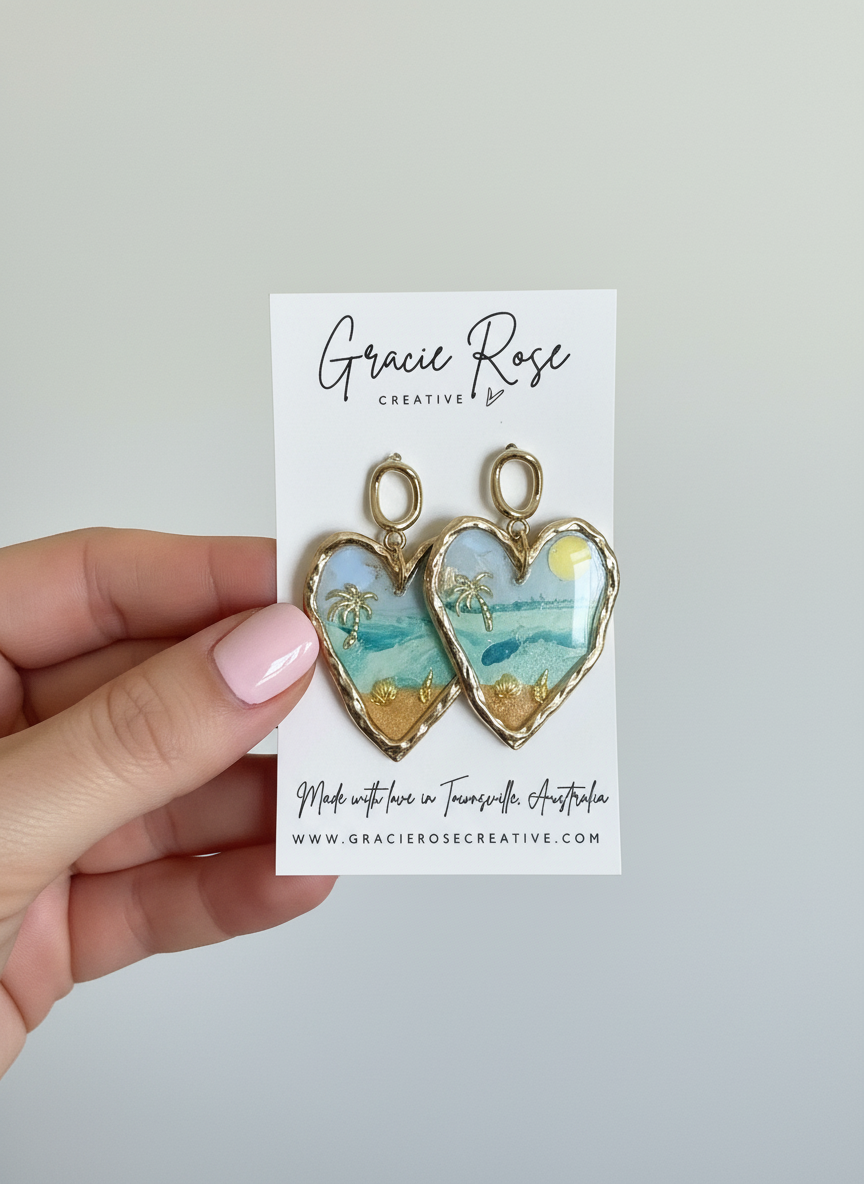 Handmade Ocean Crush Hearts earrings by Gracie Rose Creative, featuring a vibrant ocean scene with palm accents and golden details, displayed on a branded card.