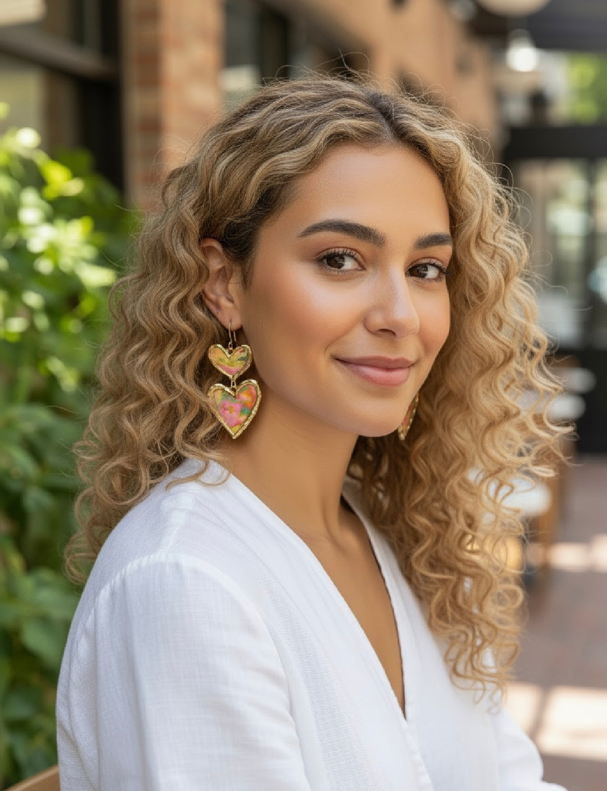 Model wearing Cross Your Heart floral earrings by Gracie Rose Creative, showcasing a stylish look with curly hair outdoors.